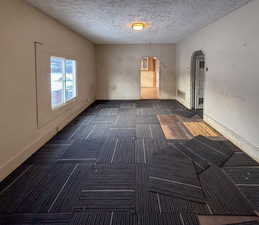 Carpeted empty room featuring arched walkways and a textured ceiling