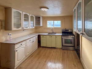 Kitchen with glass insert cabinets, a textured ceiling, gas range, light countertops, and light wood-style floors