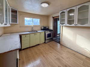 Kitchen featuring glass insert cabinets, a textured ceiling, light countertops, gas range, and light wood-style flooring