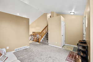 Living area featuring light colored carpet, stairway, and high vaulted ceiling