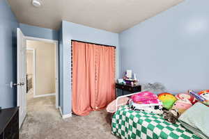 Carpeted bedroom featuring a textured ceiling and a closet