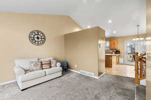 Living room featuring vaulted ceiling, a chandelier, light carpet, and recessed lighting