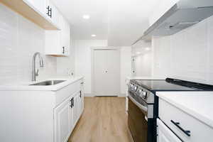 Kitchen with backsplash, stainless steel electric range, white cabinetry, extractor fan, and light wood-style floors