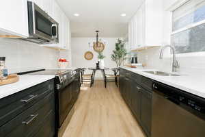 Kitchen with stainless steel appliances, white cabinetry, dark cabinets, light stone countertops, and light wood-type flooring