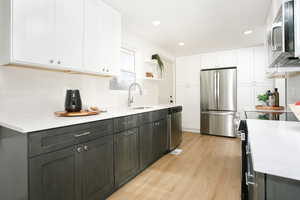 Kitchen featuring white cabinets, stainless steel appliances, light stone counters, backsplash, and recessed lighting