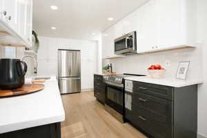 Kitchen with appliances with stainless steel finishes, white cabinetry, tasteful backsplash, light stone counters, and recessed lighting