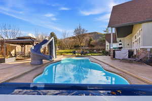 View of pool featuring a gazebo, a patio, a water slide, and a mountain view