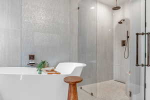 Full bathroom featuring walk in shower, a soaking tub, and tile walls