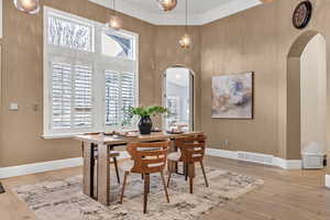 Dining space with light wood-style floors, arched walkways, and a high ceiling