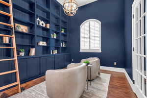 Sitting room with dark wood-style flooring, built in shelves, and a chandelier