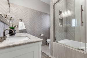 Full bath featuring double vanity, tiled shower / bath combo, and tile walls