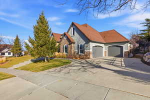 View of front facade featuring stone siding, stucco siding, concrete driveway, a front lawn, and roof with shingles