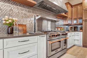 Kitchen featuring range with two ovens, custom exhaust hood, tasteful backsplash, and white cabinets