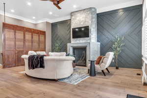 Living room with ornamental molding, light wood-style flooring, a fireplace, an accent wall, and recessed lighting