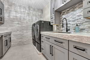 Kitchen with gray cabinetry, washing machine and clothes dryer, and light stone counters