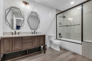 Full bathroom featuring combined bath / shower with glass door, double vanity, and light wood-type flooring