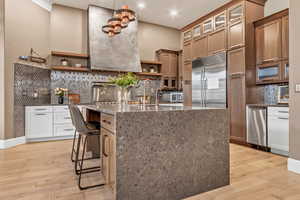 Kitchen featuring open shelves, tasteful backsplash, light wood finished floors, dark stone countertops, and appliances with stainless steel finishes