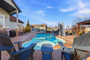 View of swimming pool with an outdoor structure, a patio, a water slide, a storage structure, and a grill