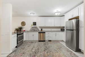 Kitchen featuring white cabinetry, appliances with stainless steel finishes, and light stone countertops
