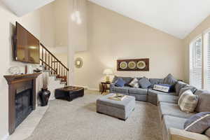 Carpeted living room with high vaulted ceiling, a fireplace with flush hearth, and stairway