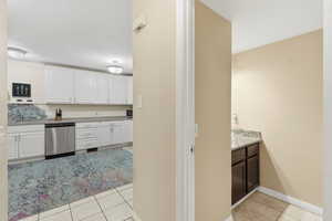 Kitchen featuring light tile patterned floors, light stone counters, dishwasher, and white cabinets