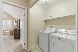 Laundry area with washer and dryer, vaulted ceiling, and light colored carpet