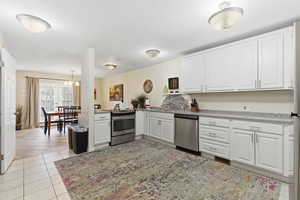 Kitchen with white cabinets, stainless steel appliances, light tile patterned floors, a chandelier, and a peninsula