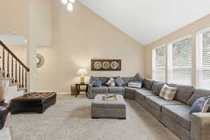 Living area with high vaulted ceiling, carpet flooring, and stairs