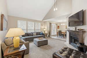 Living room featuring high vaulted ceiling, a fireplace with flush hearth, carpet, and a chandelier