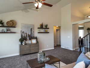 Living room with carpet flooring, high vaulted ceiling, ceiling fan, and stairs