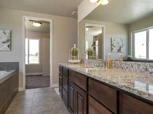 Full bath featuring vanity, plenty of natural light, tiled bath, light tile patterned flooring, and a textured ceiling