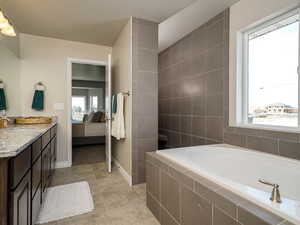 Ensuite bathroom featuring a garden tub, light tile patterned flooring, and vanity