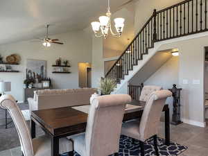 Dining room featuring stairs, tile patterned floors, high vaulted ceiling, a chandelier, and ceiling fan