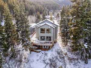 Snow covered property featuring a wooden deck and a view of trees