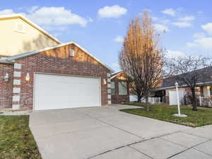 View of front of home with a front lawn, brick siding, concrete driveway, and an attached garage