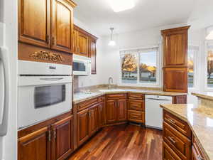 Kitchen featuring white appliances, pendant lighting, light stone countertops, dark wood-style floors, and brown cabinets