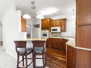 Kitchen with a breakfast bar area, white appliances, brown cabinets, backsplash, and hanging light fixtures