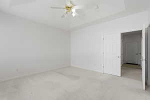 Unfurnished room with light carpet, ceiling fan, and a tray ceiling
