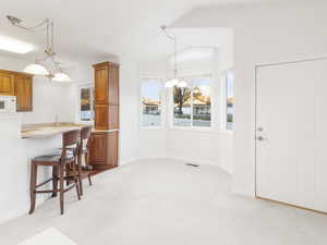 Kitchen featuring a kitchen bar, hanging light fixtures, light colored carpet, brown cabinetry, and healthy amount of natural light