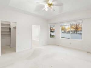 Unfurnished bedroom with a walk in closet, light carpet, a tray ceiling, a ceiling fan, and ensuite bathroom
