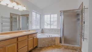 Bathroom featuring a towel warming rack, vaulted ceiling, a shower stall, double vanity, and a bath