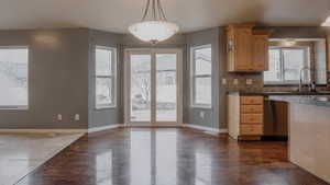 Kitchen with dark wood-style flooring, tile countertops, backsplash, stainless steel dishwasher, and hanging light fixtures