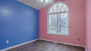 Empty room featuring dark wood-type flooring, lofted ceiling, and ceiling fan
