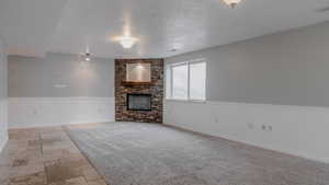 Unfurnished living room with a fireplace, stone tile flooring, light colored carpet, and wainscoting