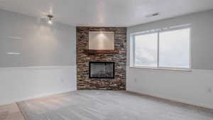Unfurnished living room featuring a stone fireplace and carpet