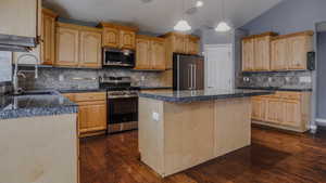Kitchen with tile counters, vaulted ceiling, appliances with stainless steel finishes, decorative light fixtures, and tasteful backsplash