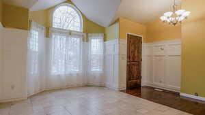 Unfurnished dining area with a decorative wall, a chandelier, a wainscoted wall, and lofted ceiling