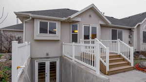 Back of property featuring roof with shingles, stucco siding, and a deck
