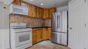 Kitchen featuring white appliances, tasteful backsplash, tile counters, stone tile flooring, and brown cabinets