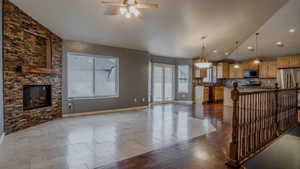 Kitchen with lofted ceiling, dark tile patterned floors, open floor plan, a stone fireplace, and hanging light fixtures